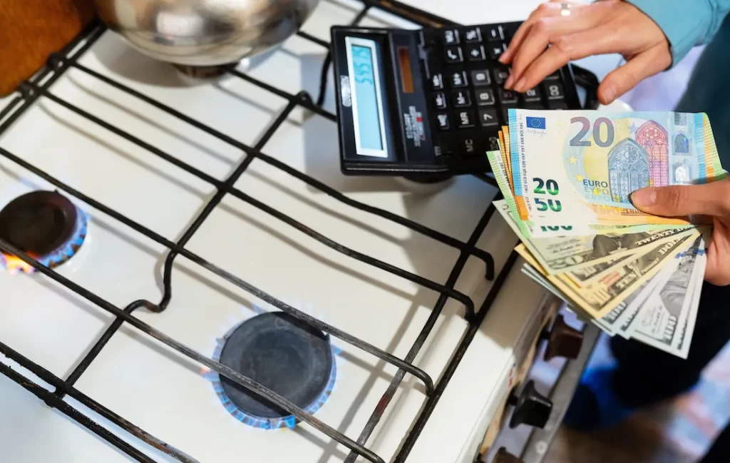 Fornello a gas acceso visto dall’alto, mentre una persona tiene in mano un ventaglio di banconote