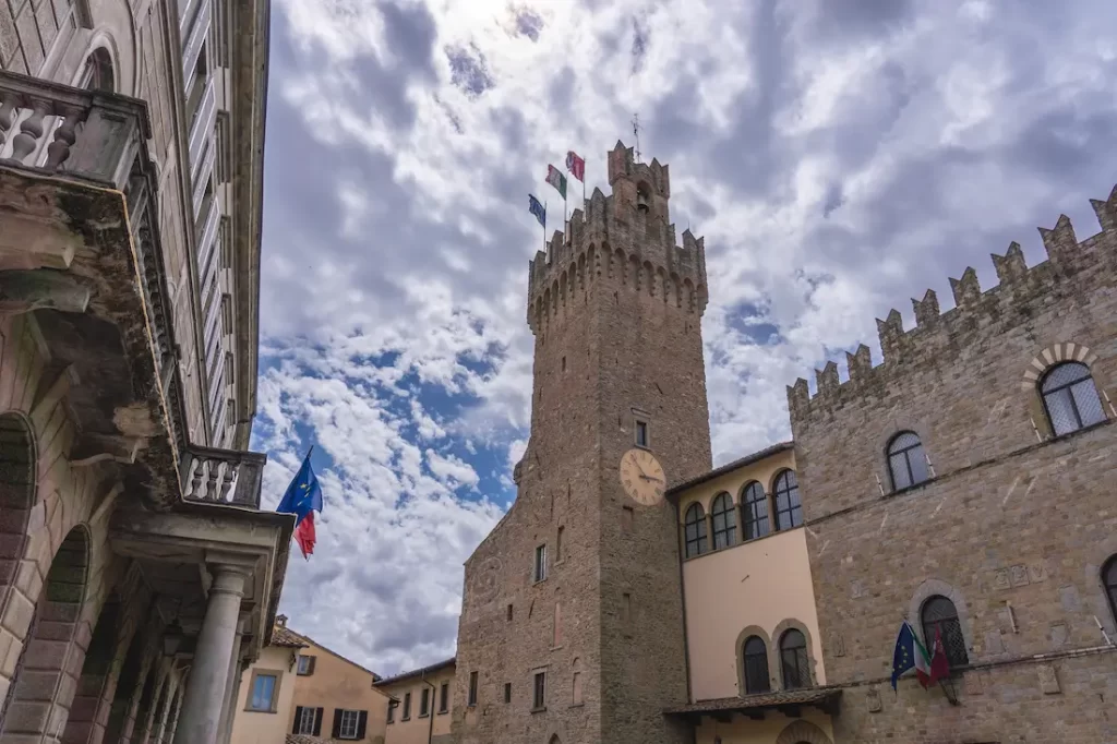 vista dallalto verso la torre del palazzo comunale di arezzo con cielo nuvoloso e bandiere italiana ed europea