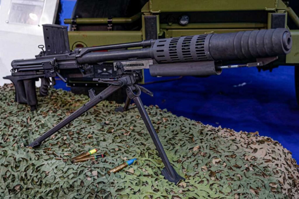 heavy machine gun mounted on a bipod resting on camouflage netting with spent shell casings nearby
