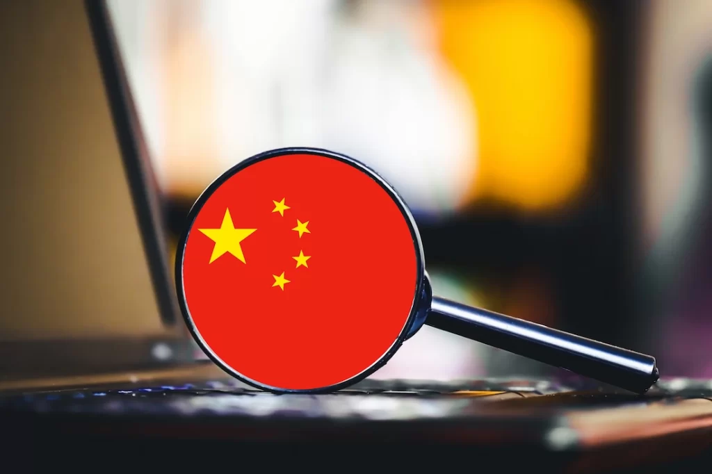 una grande lente di ingrandimento appoggiata sulla tastiera di un laptop mostra al centro la bandiera rossa della cina